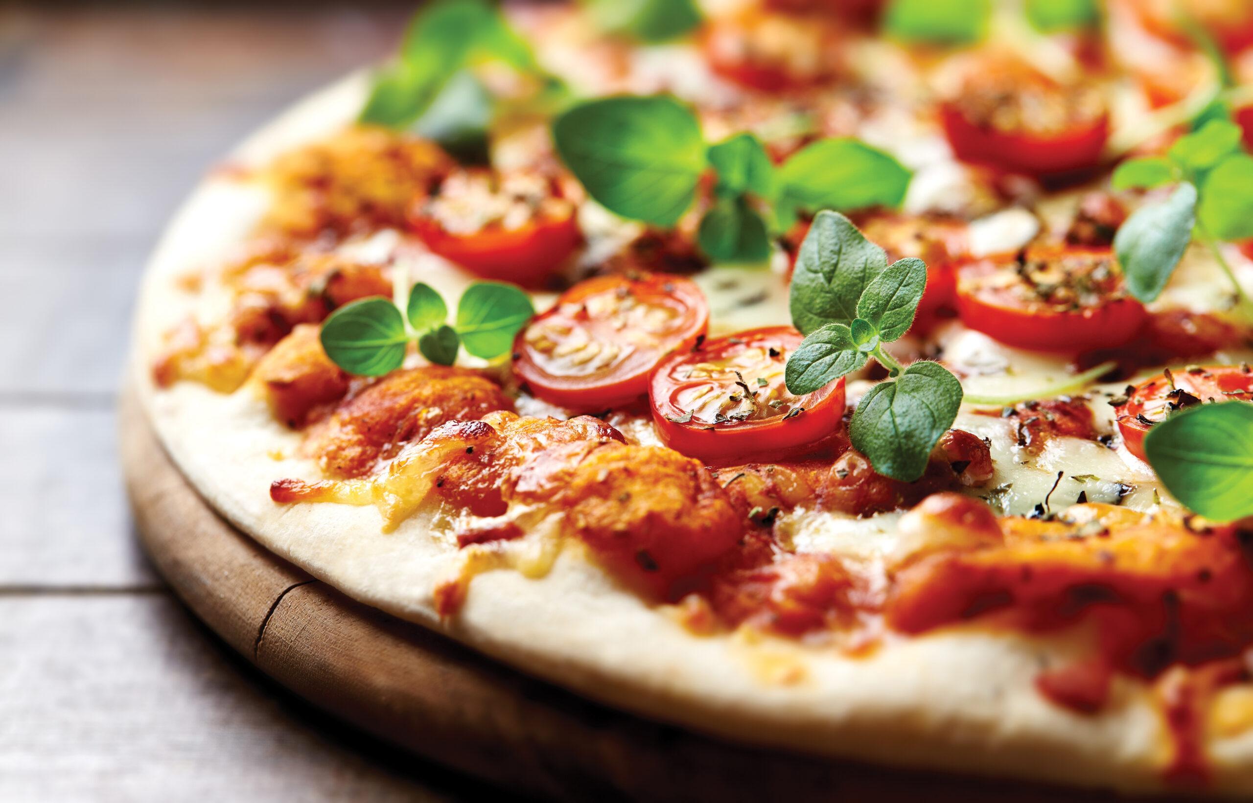 Thin-crust pizza topped with tomato slices, melted cheese, and fresh basil leaves on a wooden board.