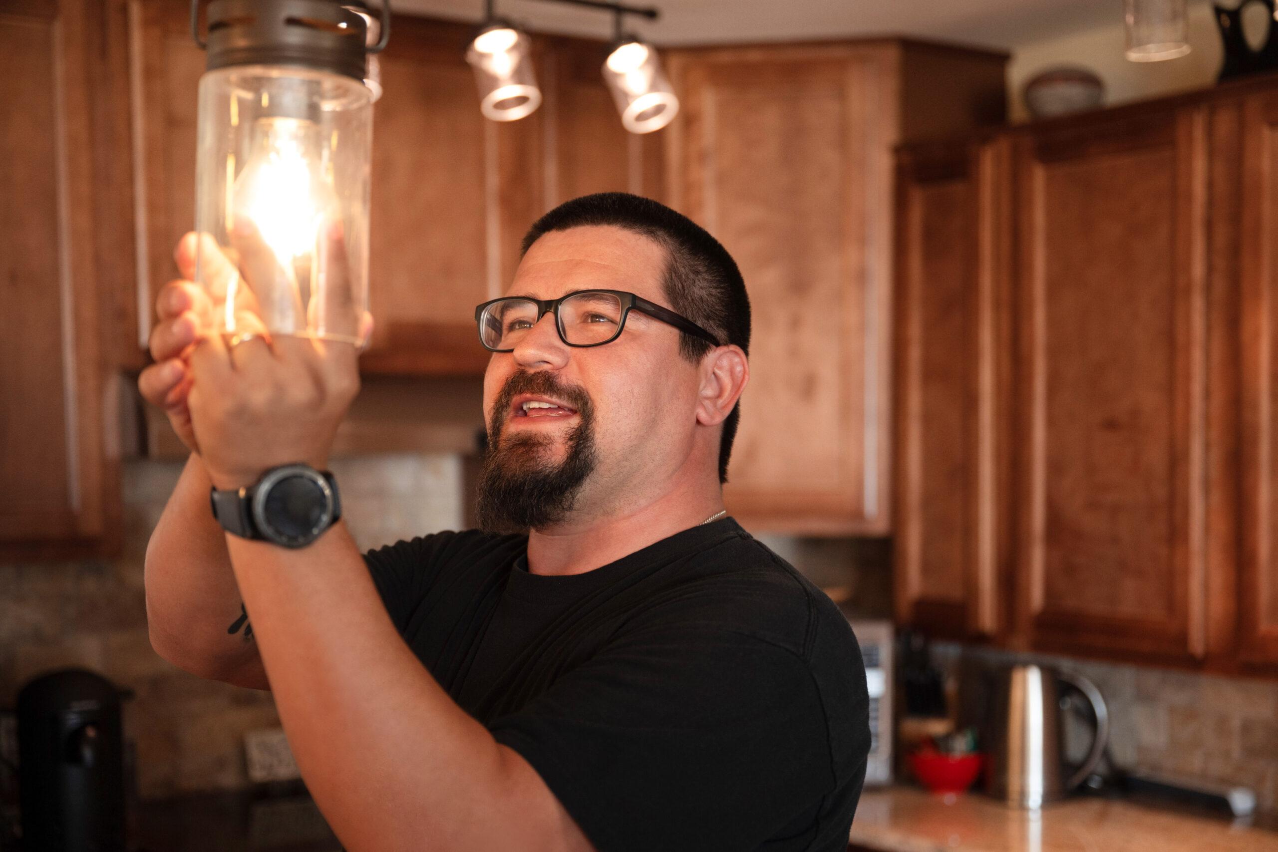 Maintenance technician adjusts a lit pendant light in a home kitchen.